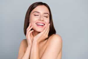A woman smiling and touching her cheeks after microneedling in Temecula, CA
